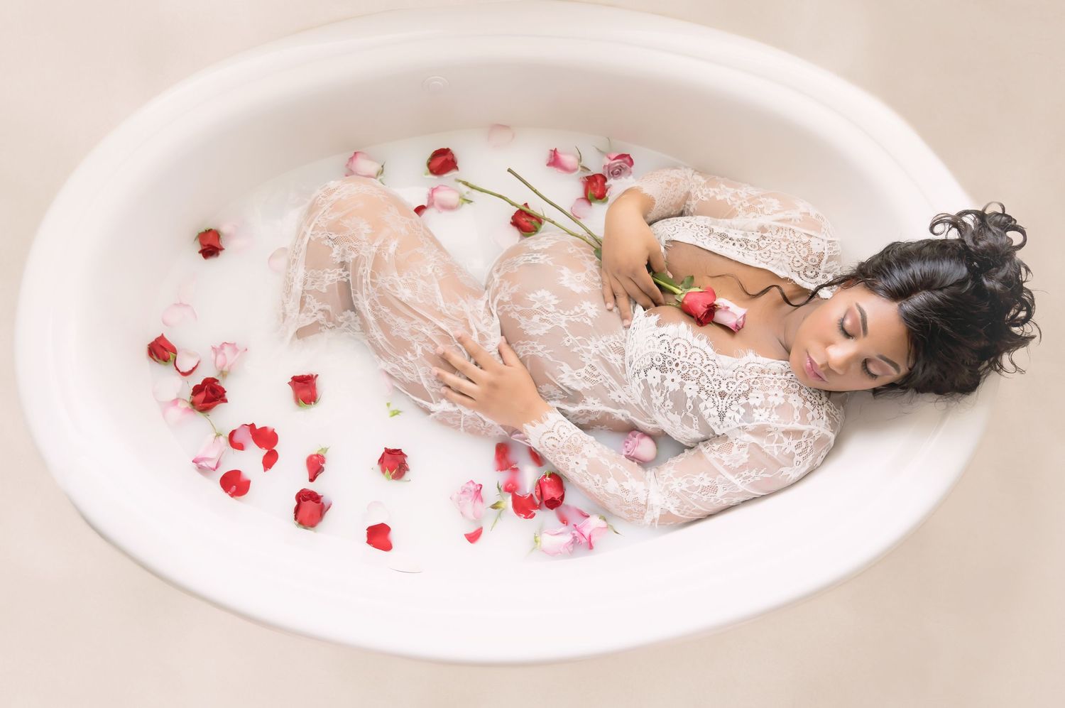 Romantic milk bath portrait with red rose petals and white lace gown.
