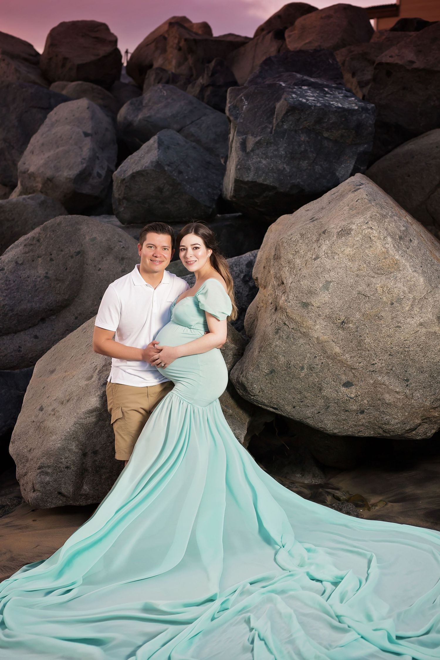 Maternity photoshoot featuring flowing mint green dress against rocky beach backdrop. San Diego Maternity Photographer