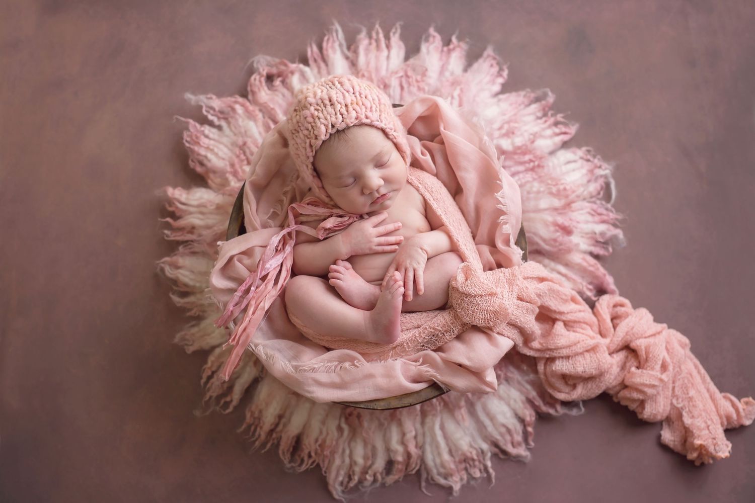 San Diego newborn photographer captures Newborn sleeping peacefully on pink fluffy blanket in professional studio setting.