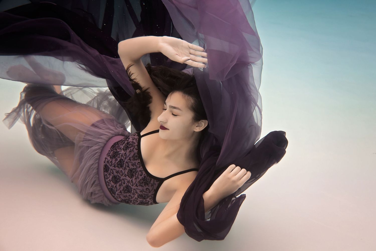 Dreamy underwater portrait with purple dress fabric drifting against pastel-toned backdrop