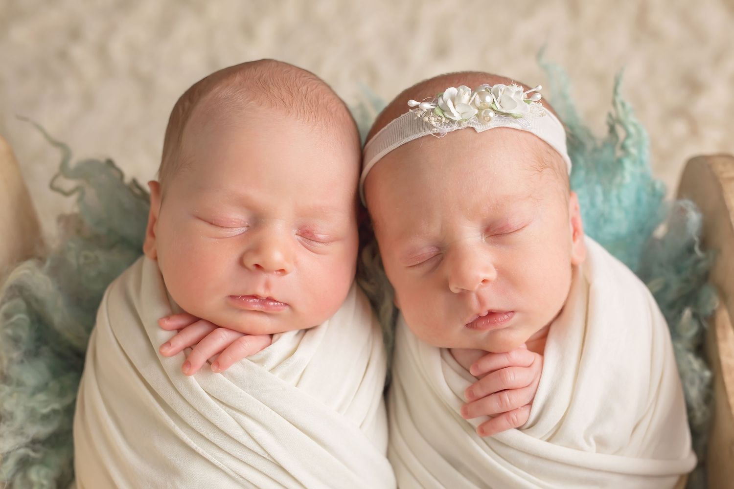 Sleeping newborn twin babies wrapped in white blankets lying side by side in a peaceful pose. San Diego Newborn Photographer