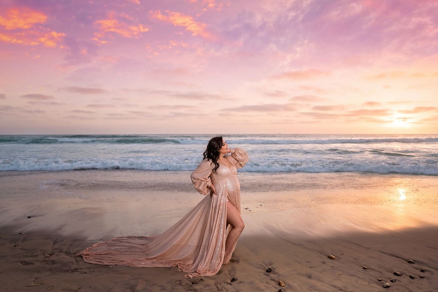 A flowing pink dress twirls on the beach during a magical sunset maternity photoshoot in san diego.