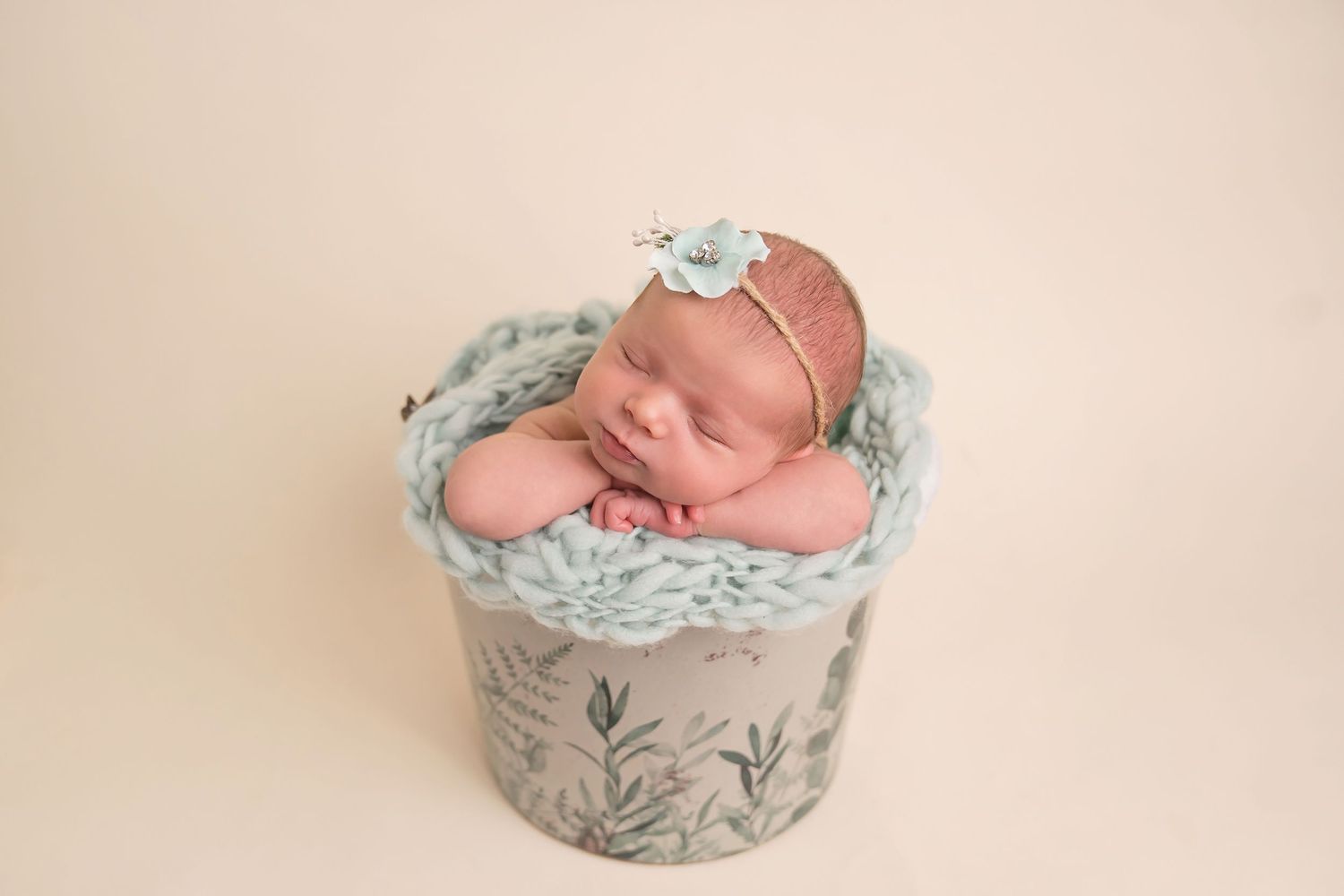 Newborn sleeping peacefully in mint green floral decorated basket against cream backdrop. San Diego Newborn Photographer