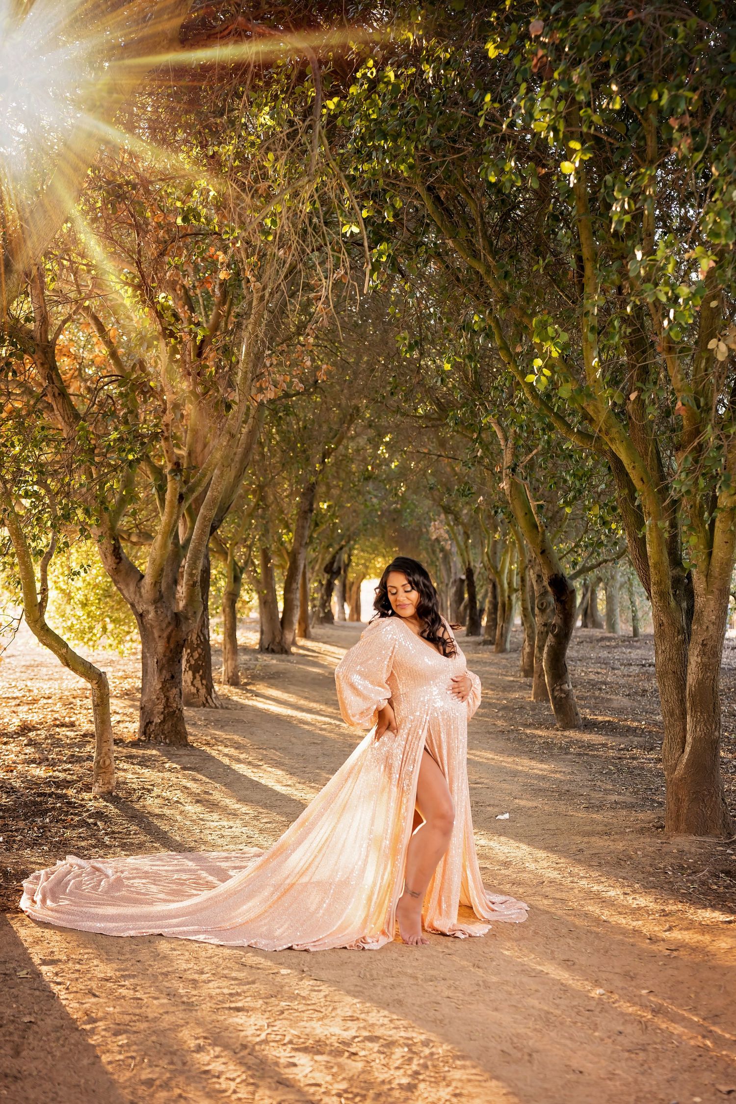 Ethereal maternity session with flowing pink gown in a sunlit forest path. San Diego Maternity Photographer