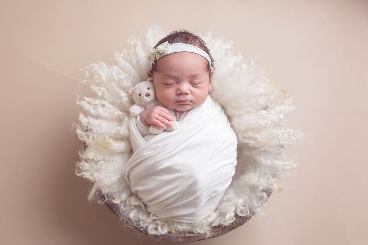 Newborn baby wrapped in white fabric lying on soft lace material in a dreamy pink setting. San Diego Newborn Photographer