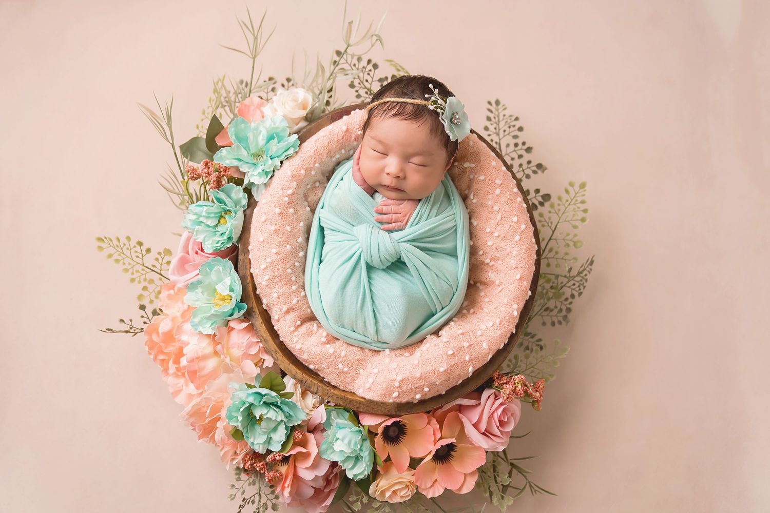 San Diego newborn photographer captures Newborn baby in mint wrap surrounded by coral and mint floral decorations.