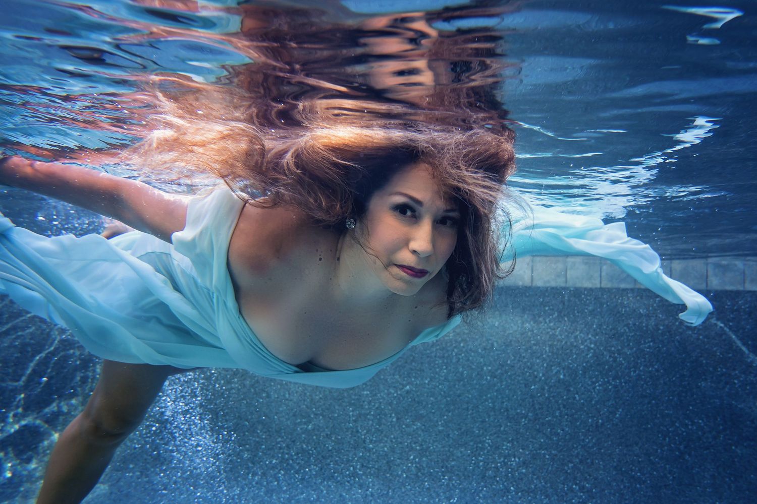 Ethereal underwater portrait with flowing fabric creating soft ripples in blue water