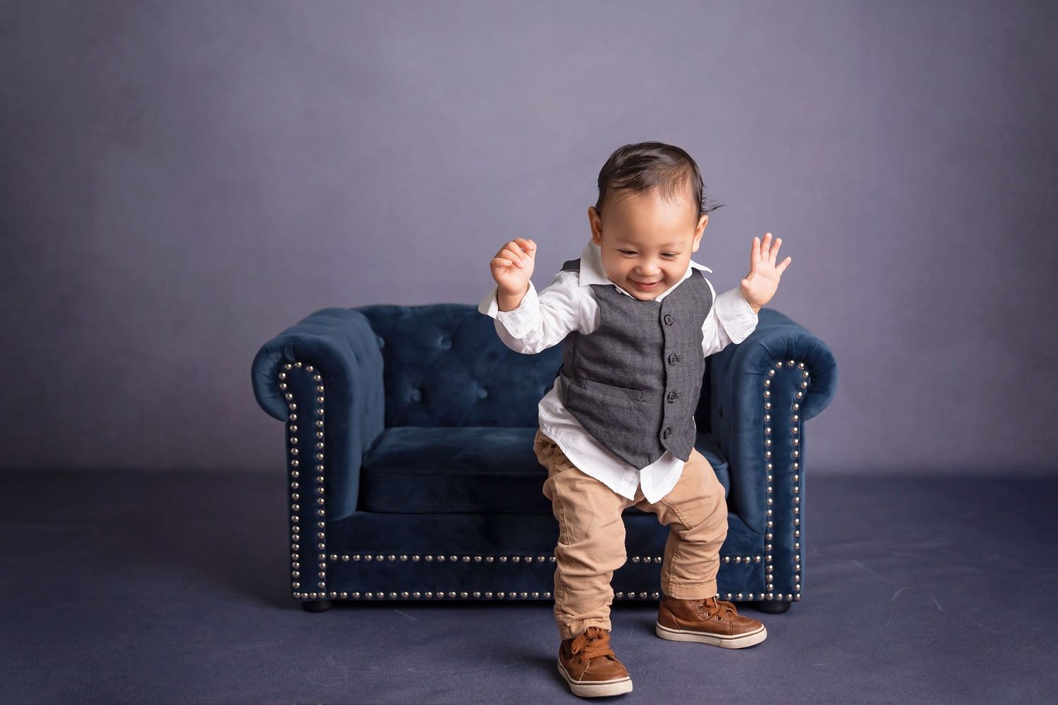 Navy blue tufted sofa against grey backdrop in studio setting.
