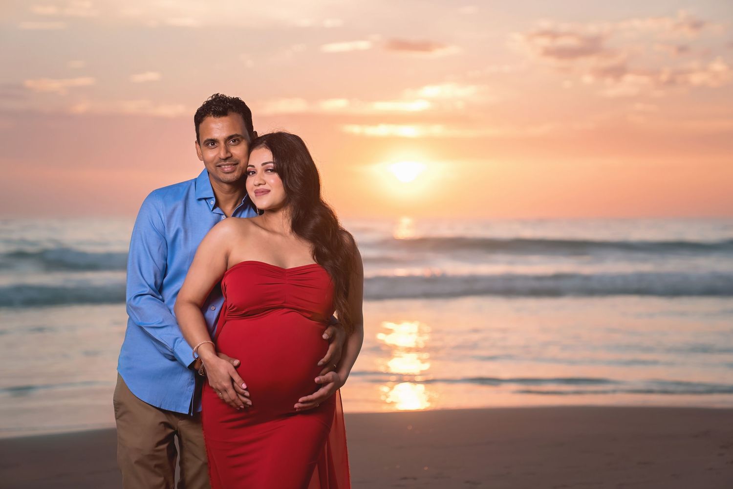 Maternity beach portrait at sunset with couple in red dress and blue shirt. San Diego Maternity Photographer