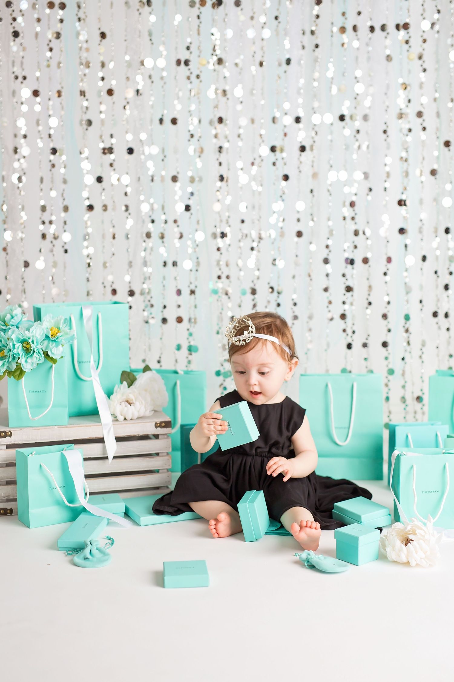 Sparkly backdrop with teal gift boxes creates glamorous portrait setting. San Diego cake smash photographer