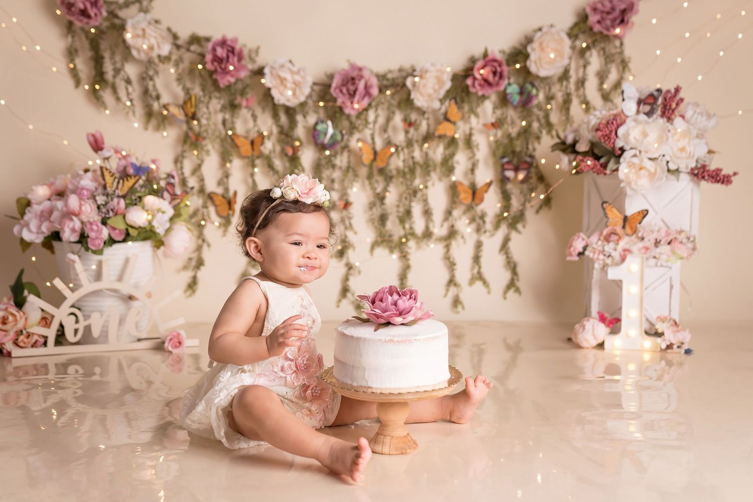 Romantic floral backdrop with pink roses and white cake display for cake smash photography.