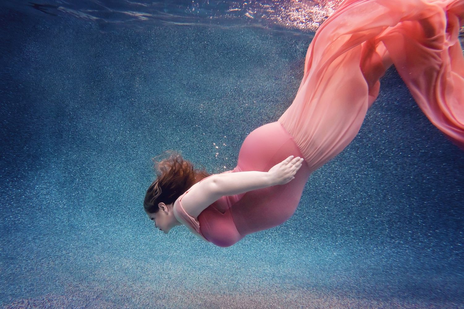 Underwater maternity portrait featuring a coral gown drifting gently with movement
