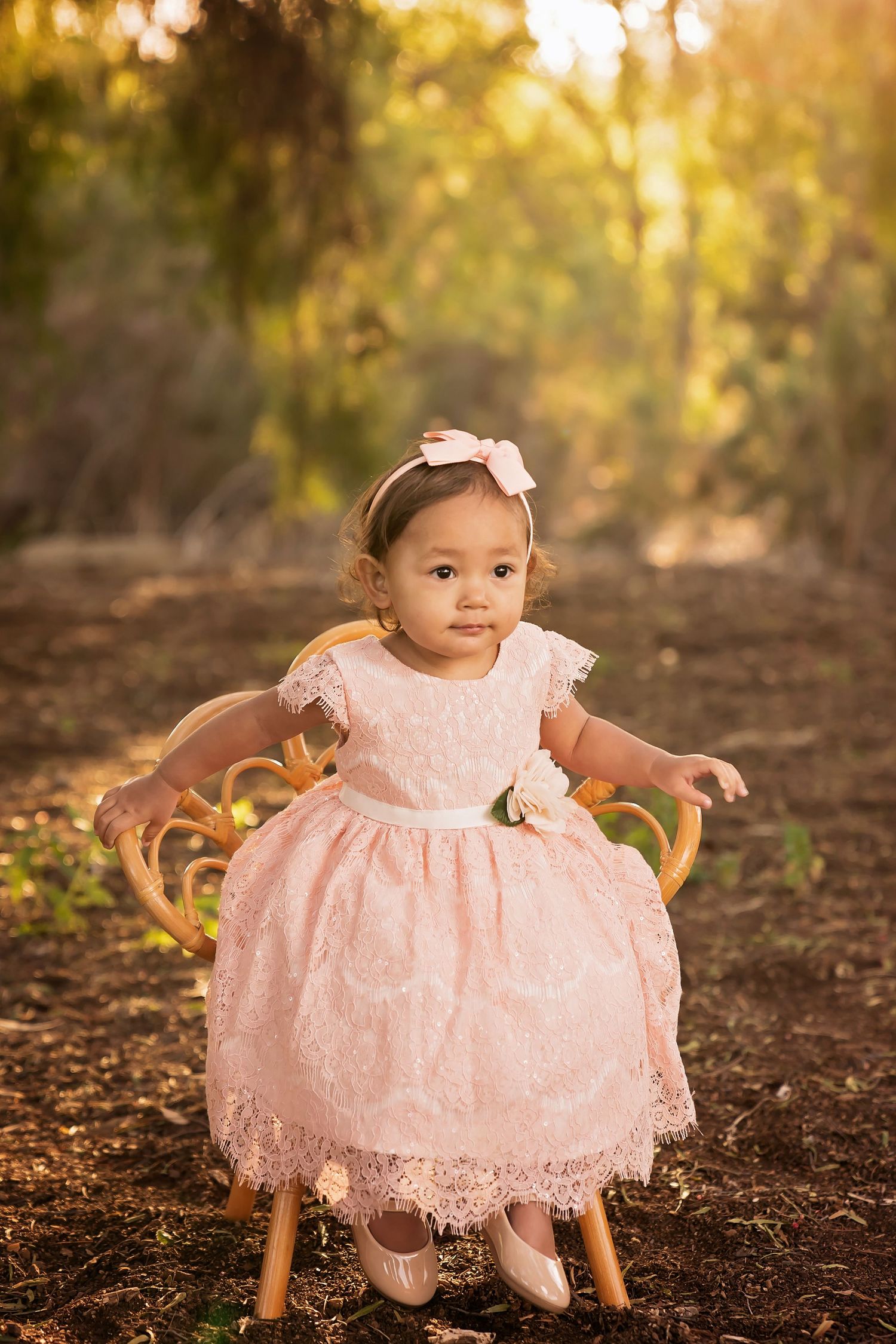 Small child in pink lace dress sitting on a wooden chair with golden sunset light behind