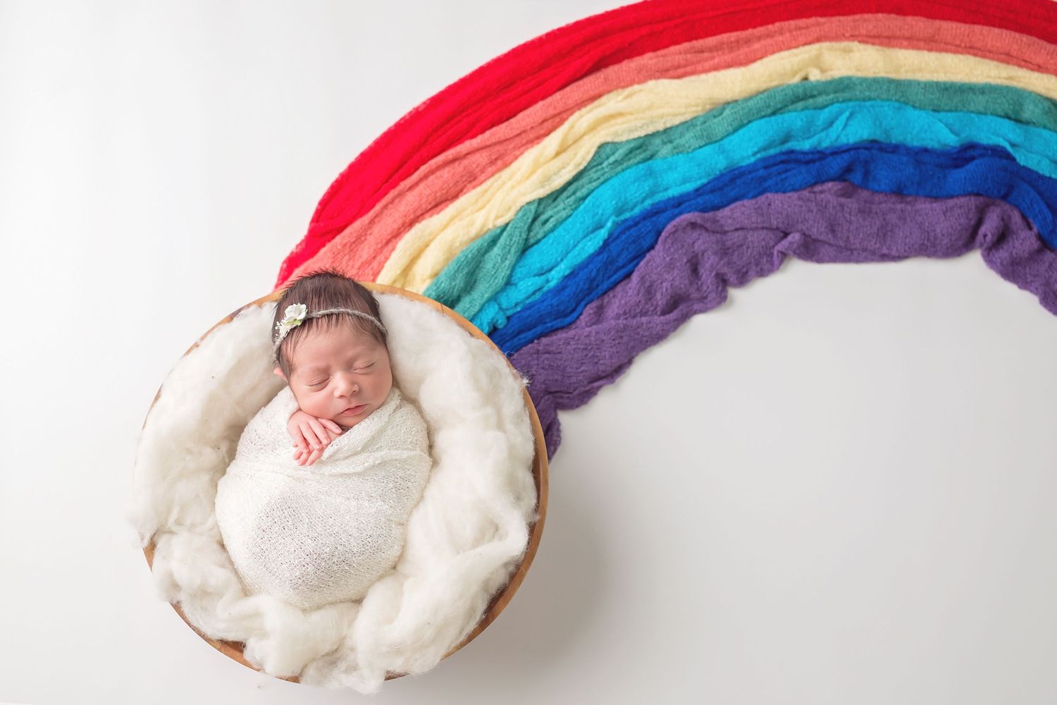 Rainbow colored fabric backdrop arranged in a soft curved shape for newborn photography. San Diego Newborn Photographer captures rainbow neb