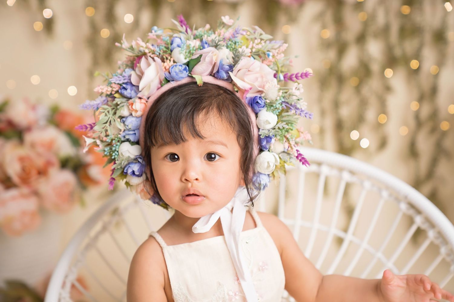 Enchanted garden photo setup with floral crown and white wicker chair.