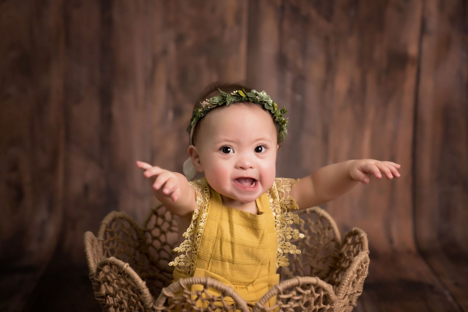 Baby wearing yellow outfit sits in woven basket surrounded by woodland decor. San Diego cake smash photographer