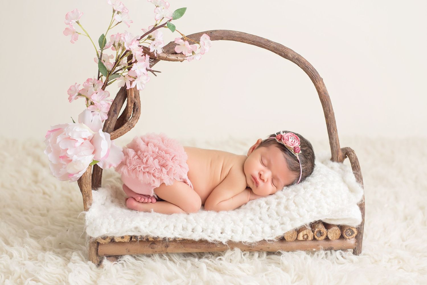 Newborn resting on wooden branch prop with delicate pink flower decorations. San Diego Newborn Photographer