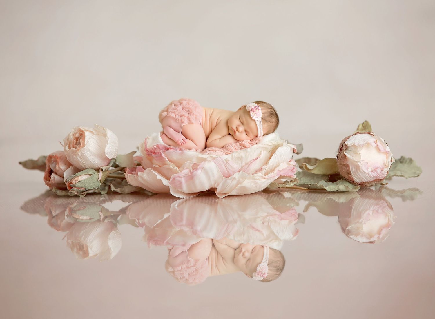 San Diego newborn photographer captures newborn baby sleeping on pink floral arrangement with soft petals against neutral background.