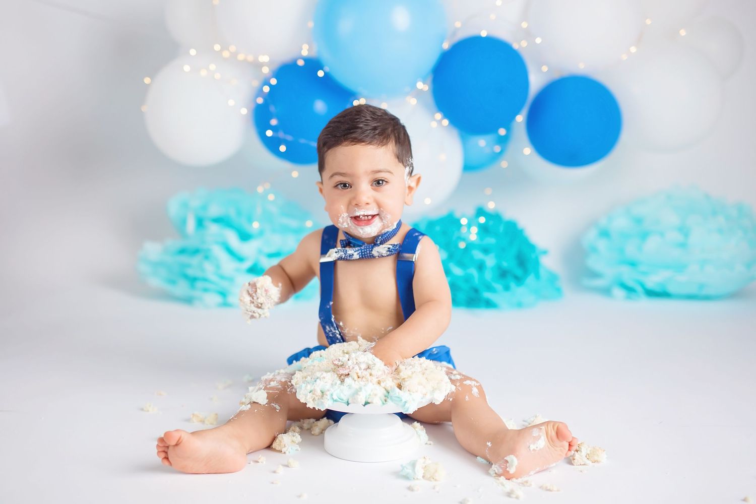 Blue and white balloon display with tissue paper decorations creates a festive photography setup. San Diego cake smash photographer