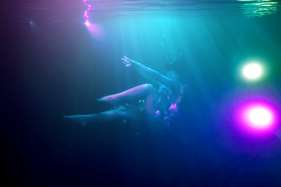 Person swimming underwater surrounded by colorful blue and pink lights in a dark aquatic environment.