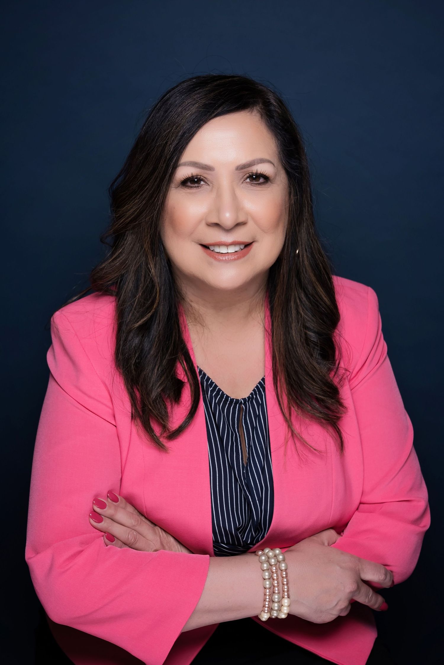 Studio portrait of woman in bright pink blazer posing warmly against dark background