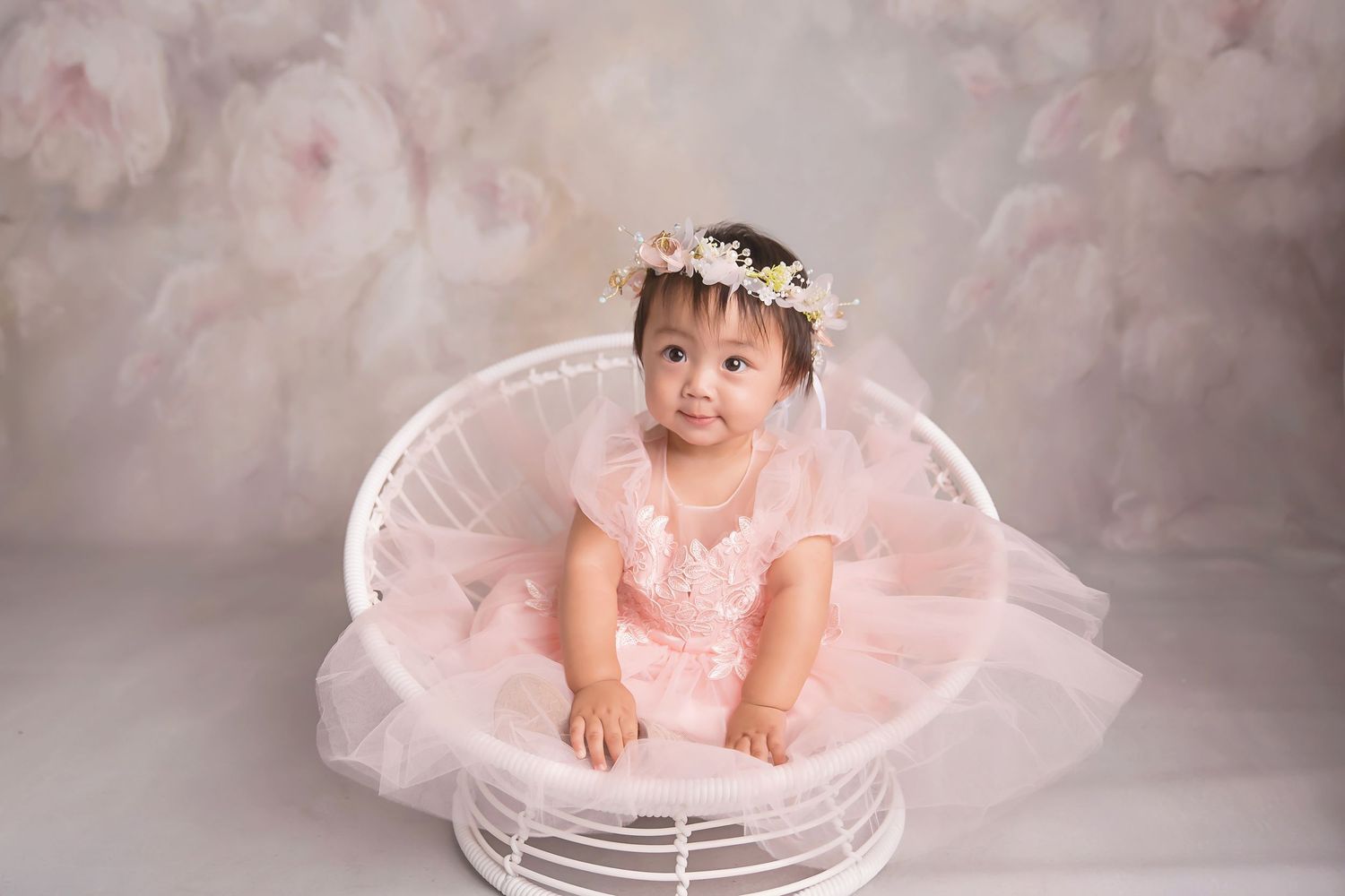 Baby portrait session in white chair with pink tulle and floral decorations.