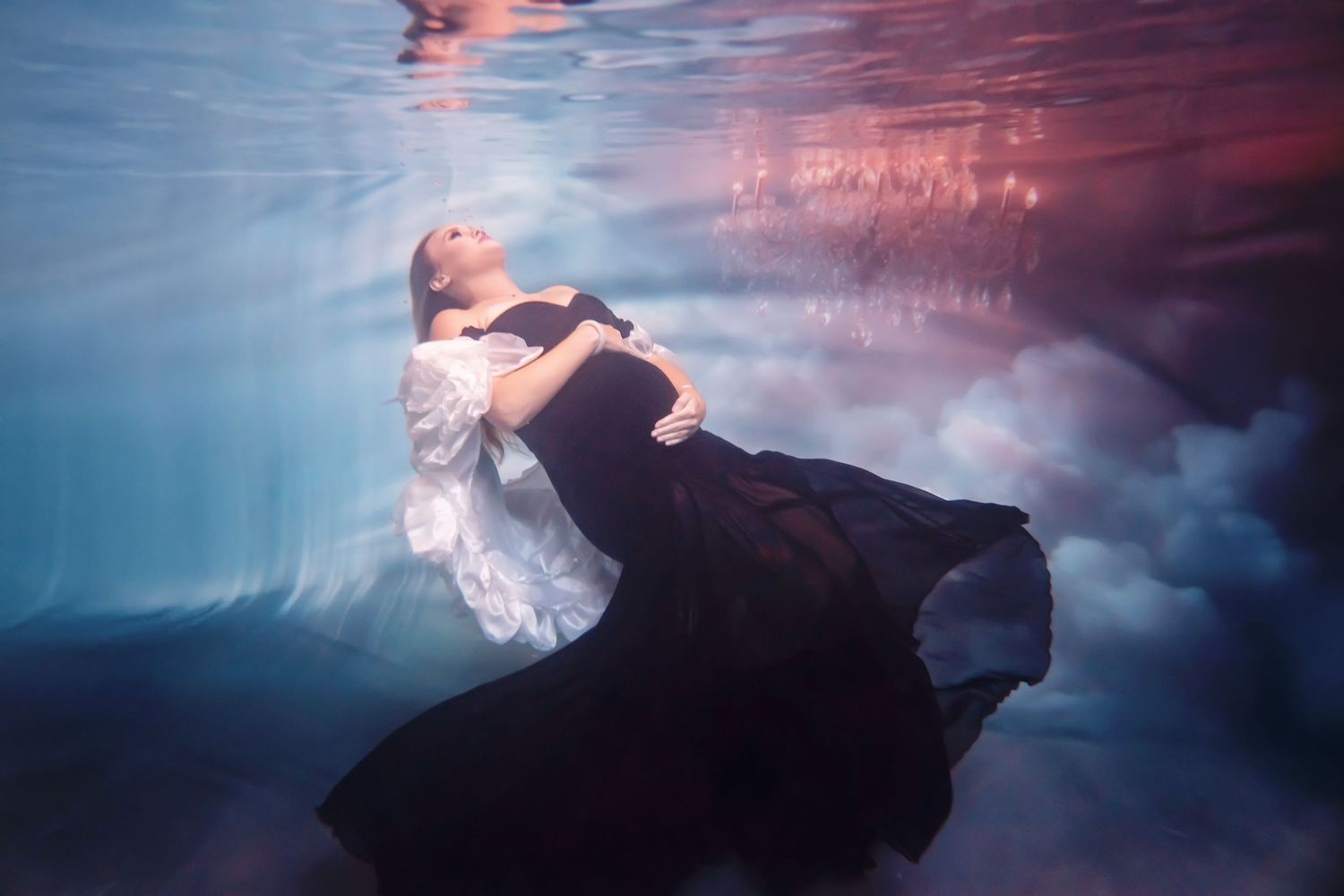 Underwater maternity portrait with flowing fabric and ethereal pink lighting
