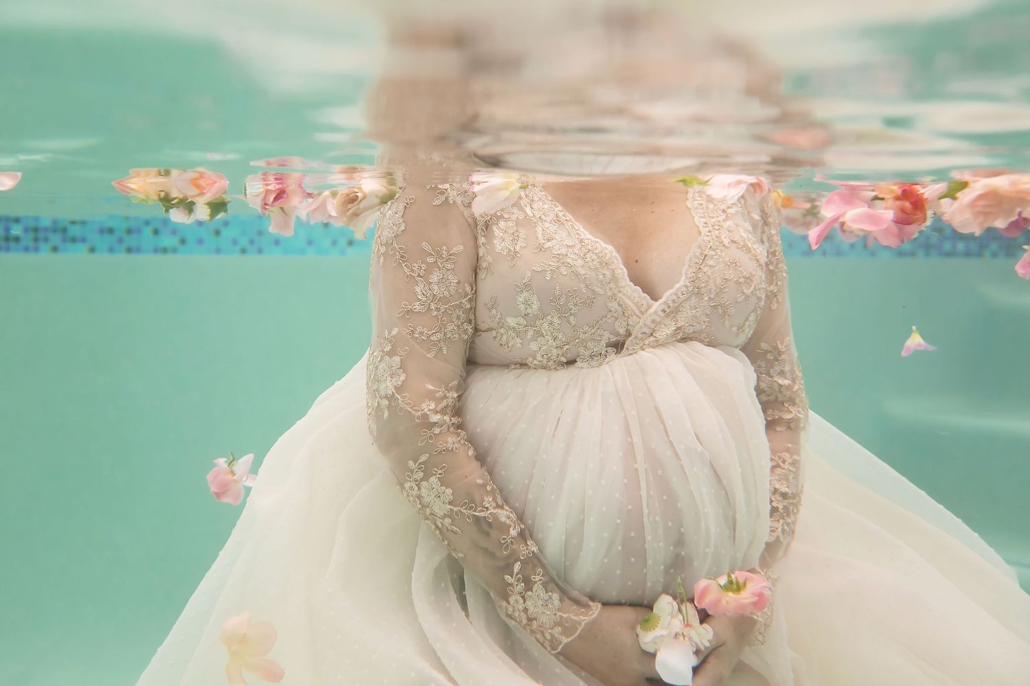 Underwater maternity portrait with white gown floating among soft flower petals