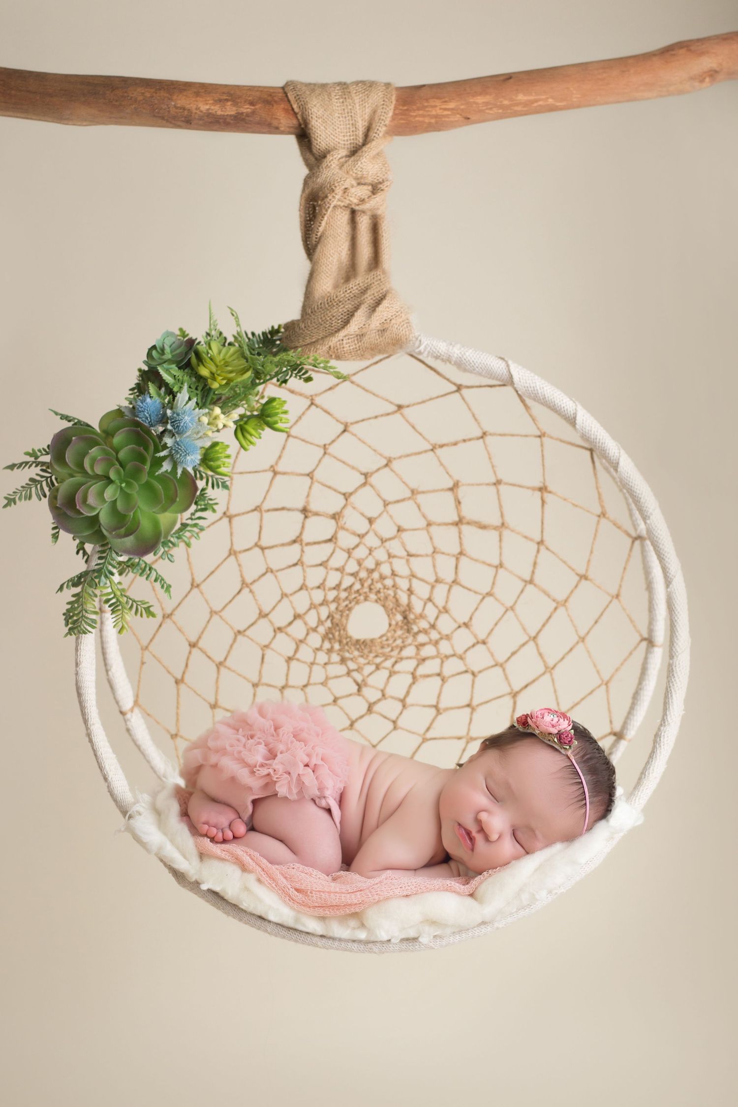 Sleeping newborn in pink wrap lying in dreamcatcher prop with floral decorations. San Diego Newborn Photographer