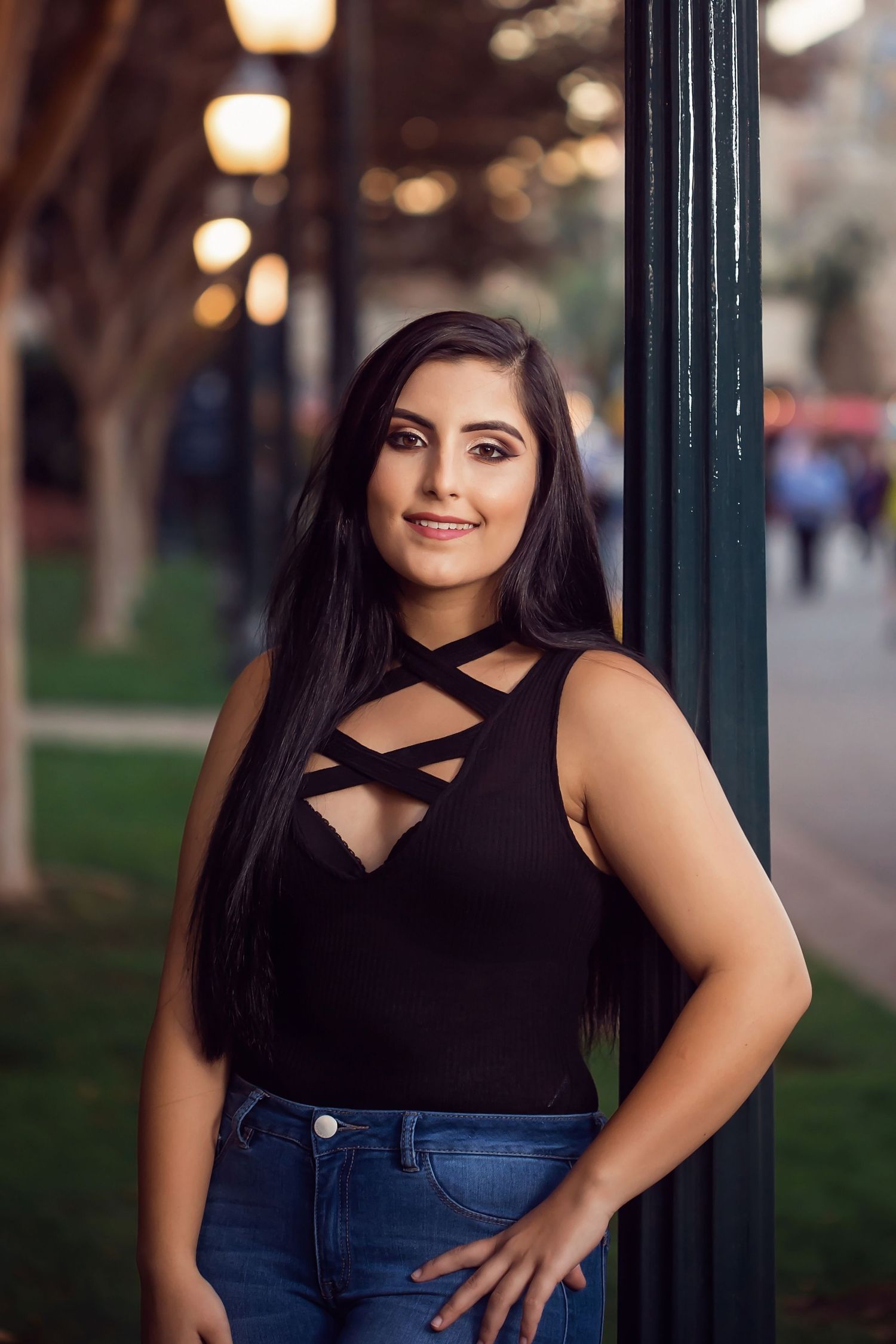 Outdoor urban headshot of woman in black top and jeans posing confidently near lampposts in San Diego