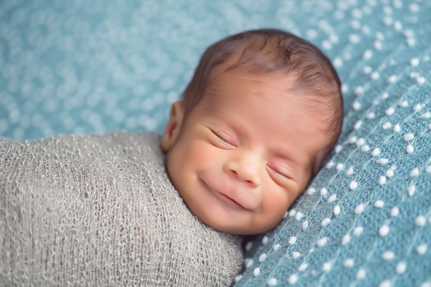 San Diego newborn photographer captures sleeping baby lies peacefully wrapped in gray knit material against a sparkly blue bokeh background.