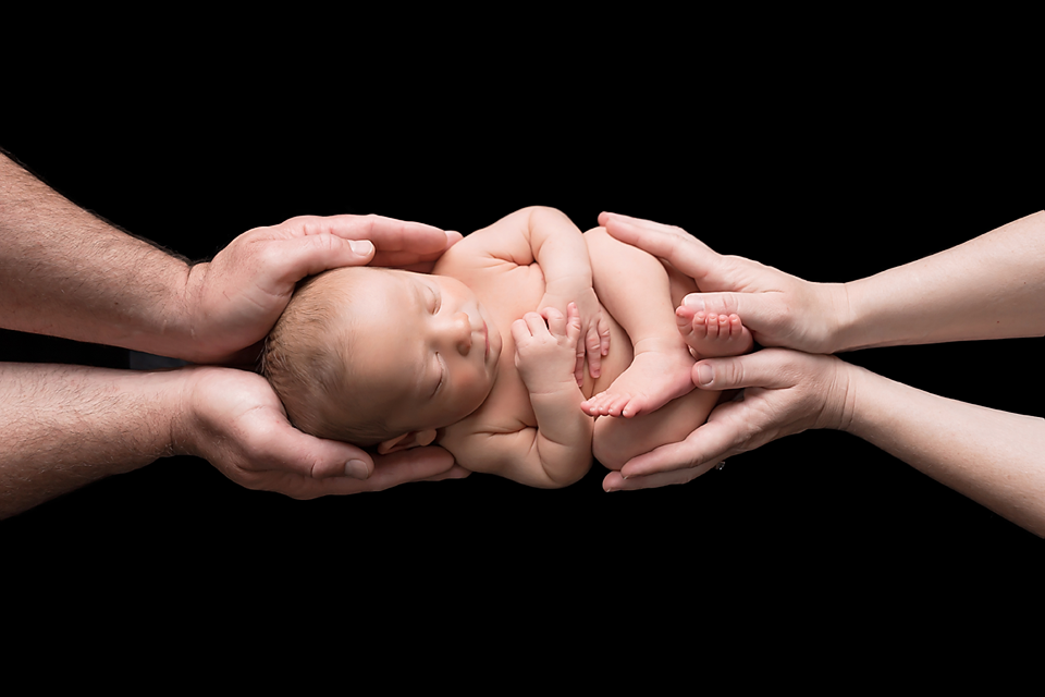 Newborn baby cradled gently in parents hands against black background, symbolizing love and new life.