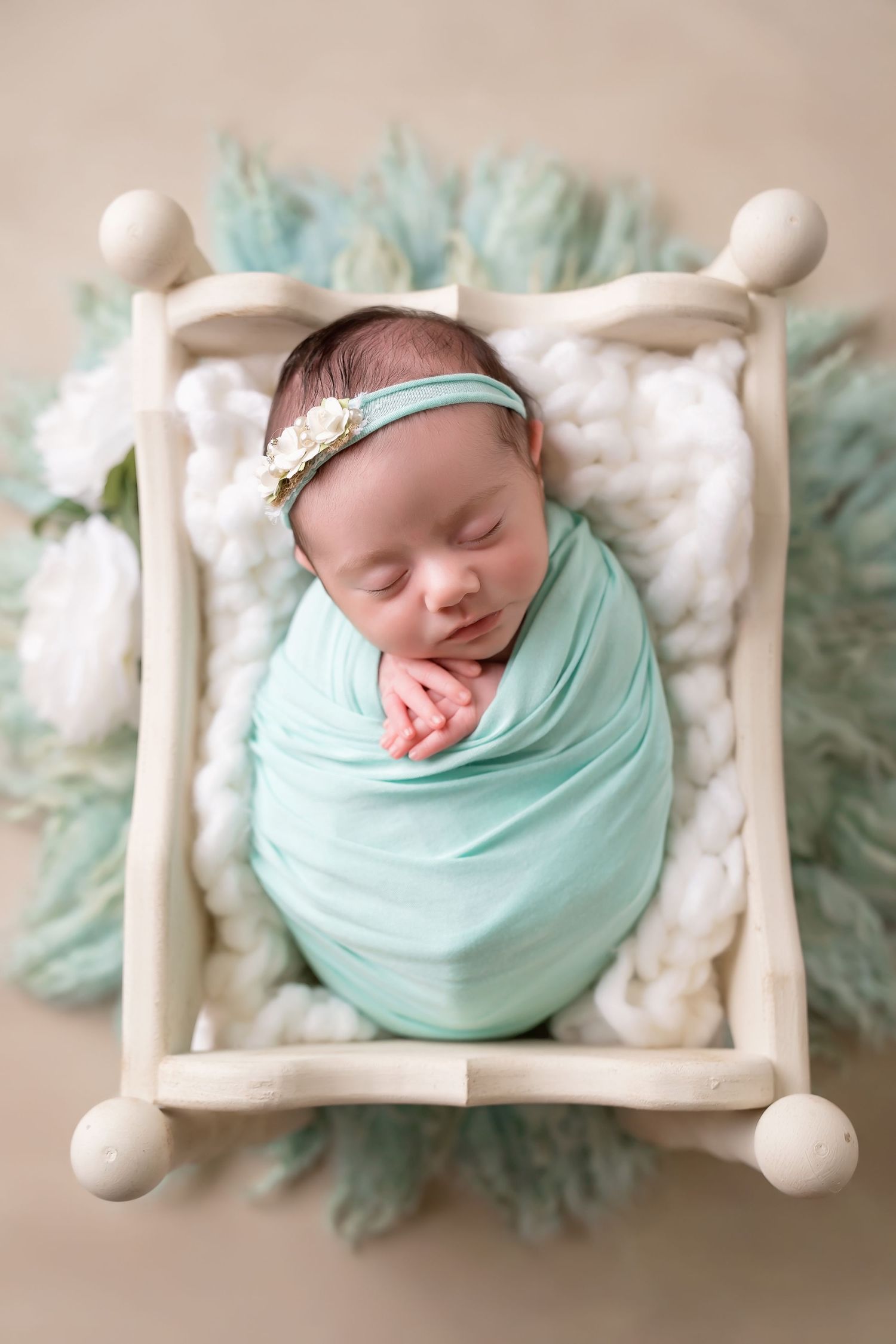 Baby sleeping on miniature white bed wrapped in mint green swaddle with floral accents. San Diego Newborn Photographer