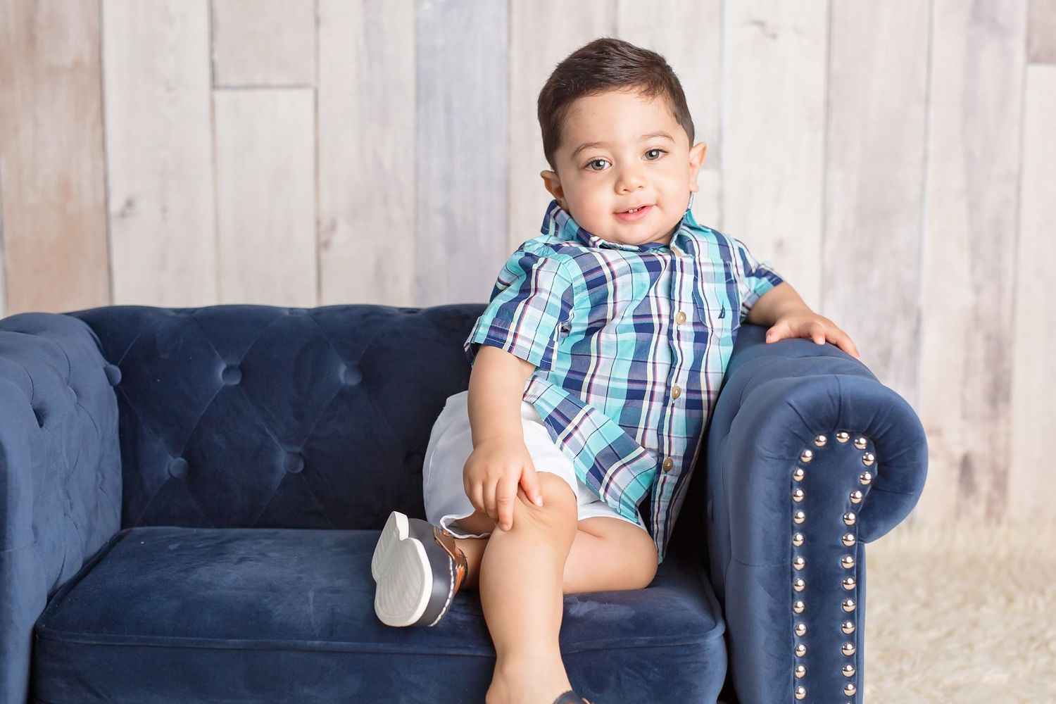Child relaxes on a navy blue tufted sofa during a casual photo session. San Diego cake smash photographer