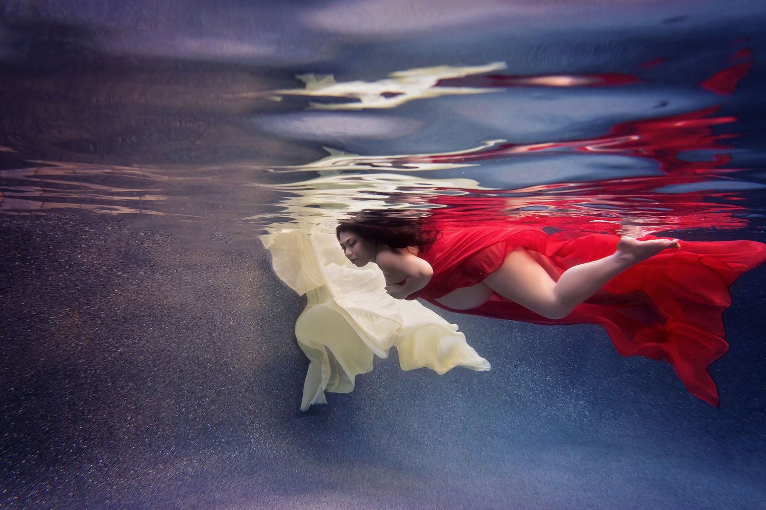 Dramatic underwater portrait featuring red and white fabrics contrasting against dark water