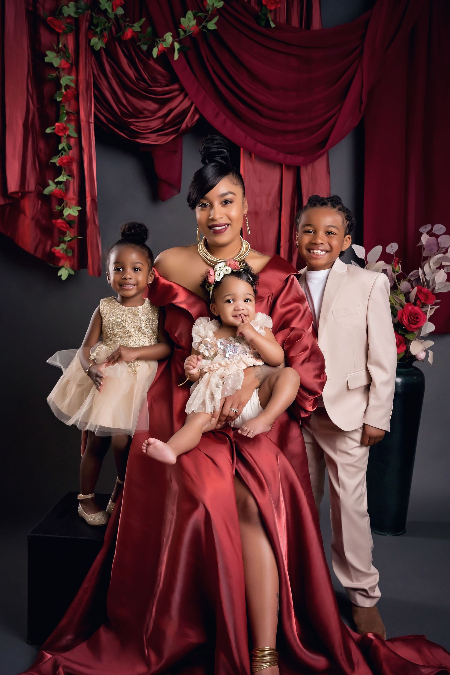 Family dressed in burgundy and cream elegant wear posed against rich red drapery
