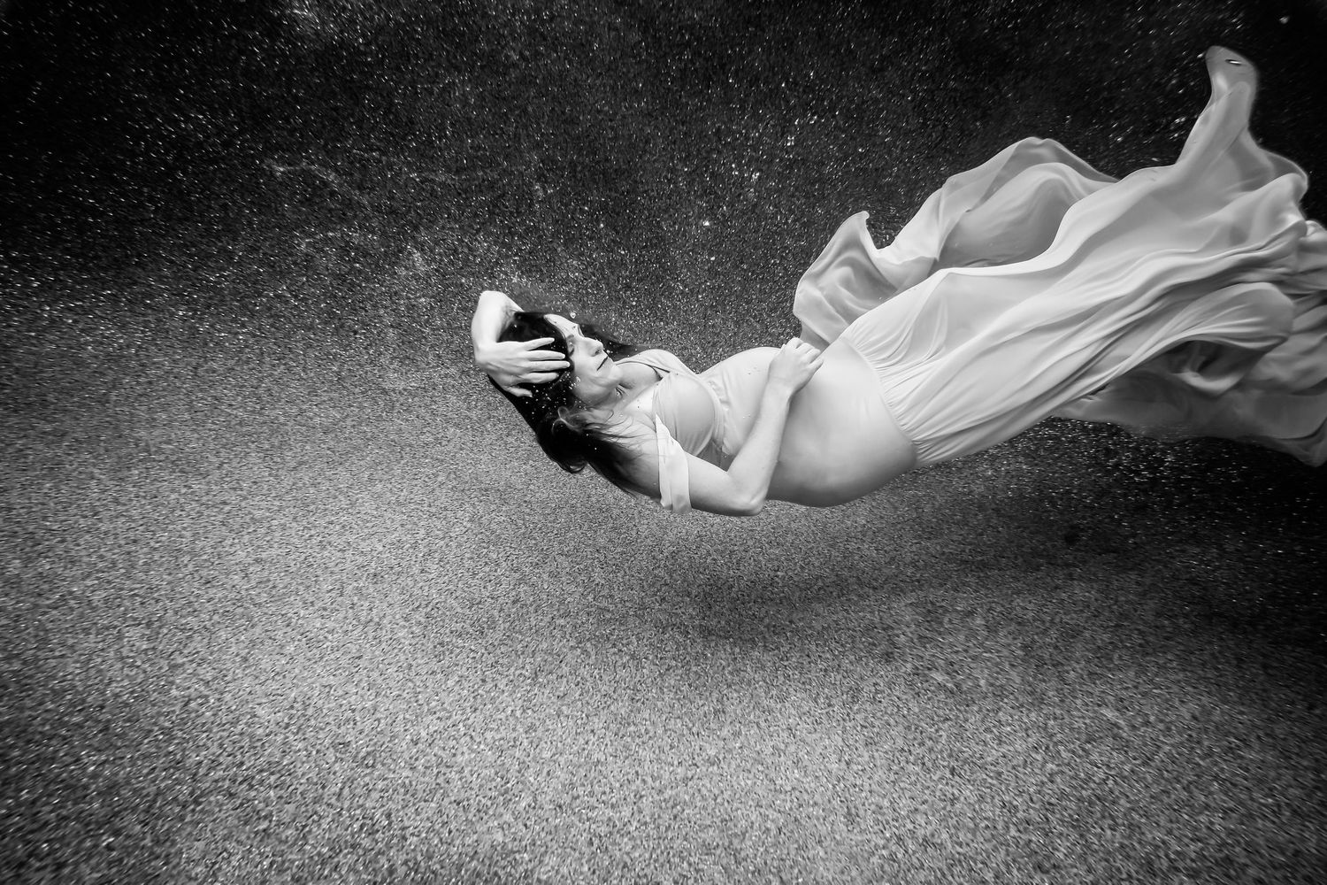 Monochrome underwater portrait featuring movement of white fabric against dark water