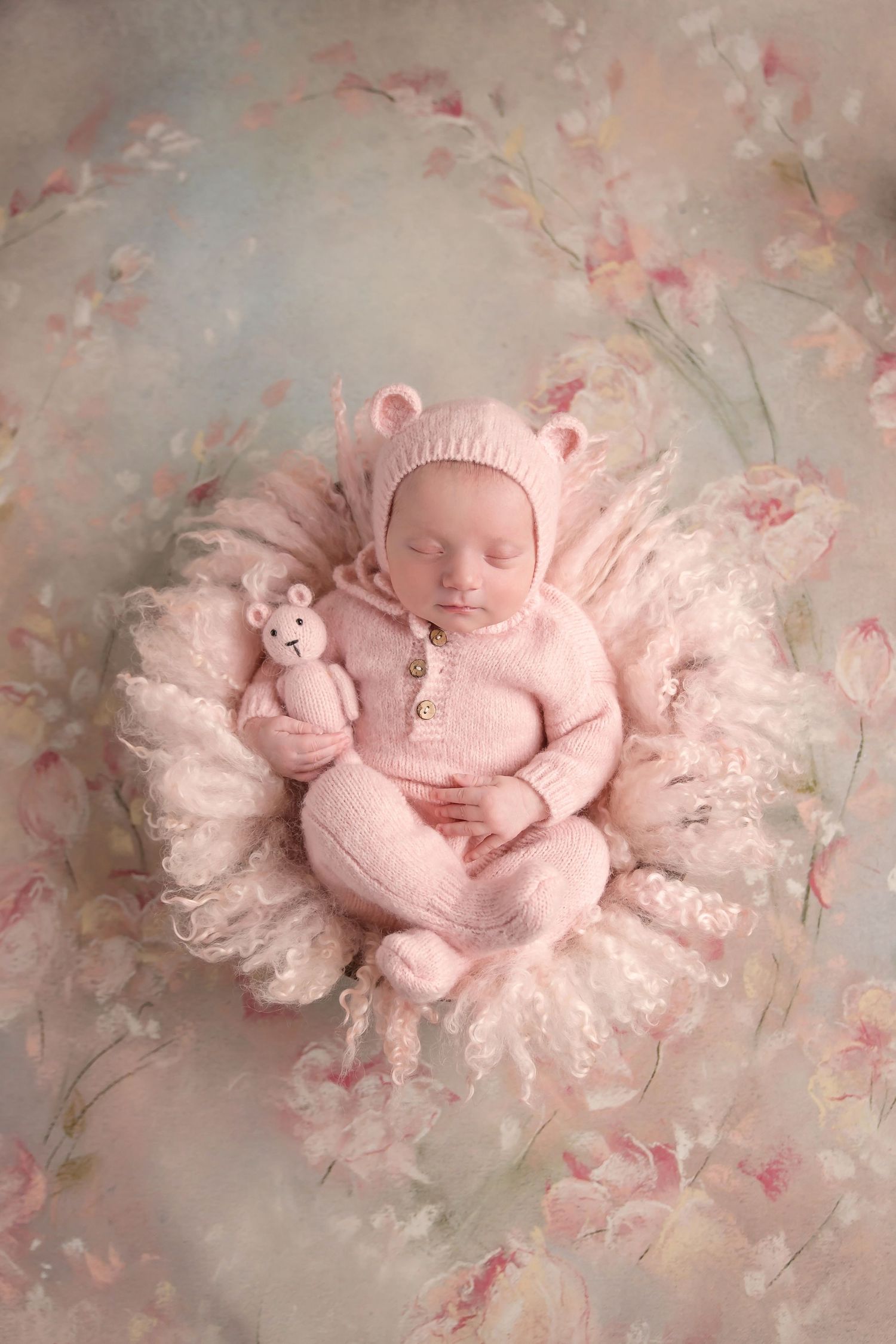 Sleeping newborn in pink knit outfit lying on lace blanket with floral background. San Diego Newborn Photographer