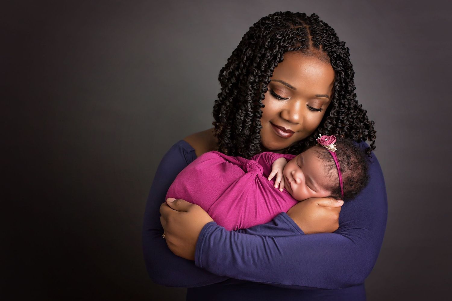 Tender moment captured in studio with baby wrapped in pink against dark background. San Diego Newborn Photographer