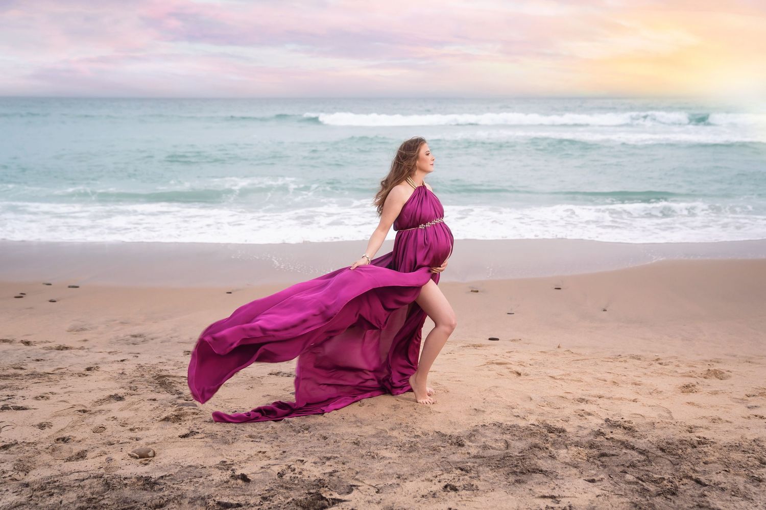 Flowing magenta dress catches wind during sunset beach maternity photoshoot. San Diego Maternity Photographer