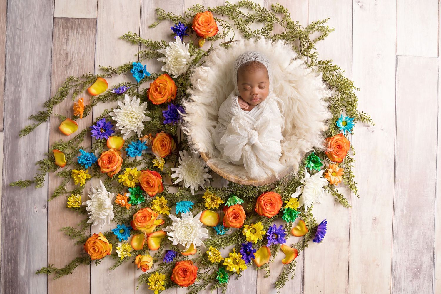 Newborn photography setup with colorful floral wreath arrangements on white wooden backdrop. San Diego Newborn Photographer