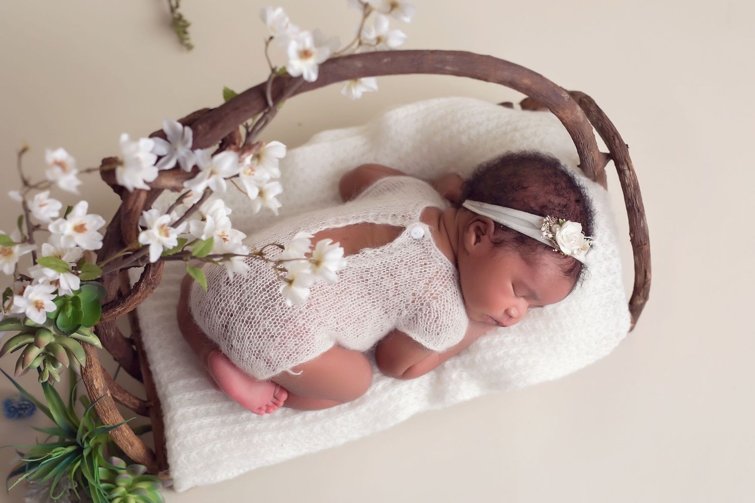 Sleeping newborn on white fabric under curved wooden branch with cherry blossoms. San Diego Newborn Photographer