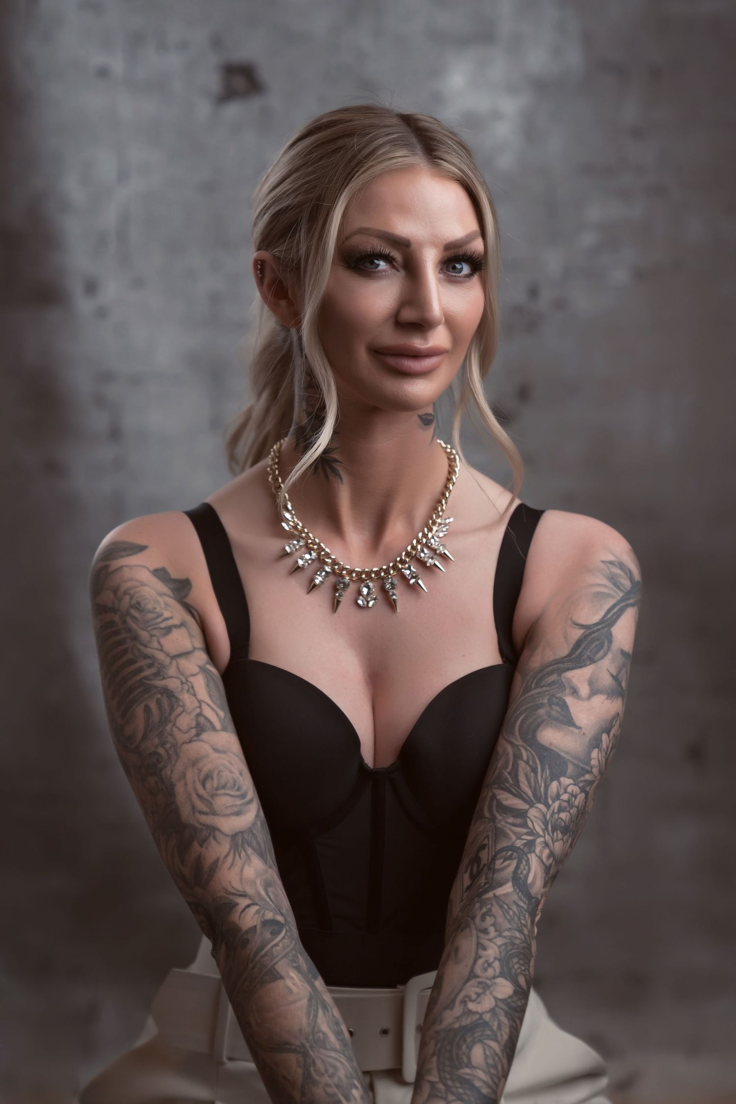 Glamour portrait showcasing woman with tattoo sleeves, statement necklace, and black top