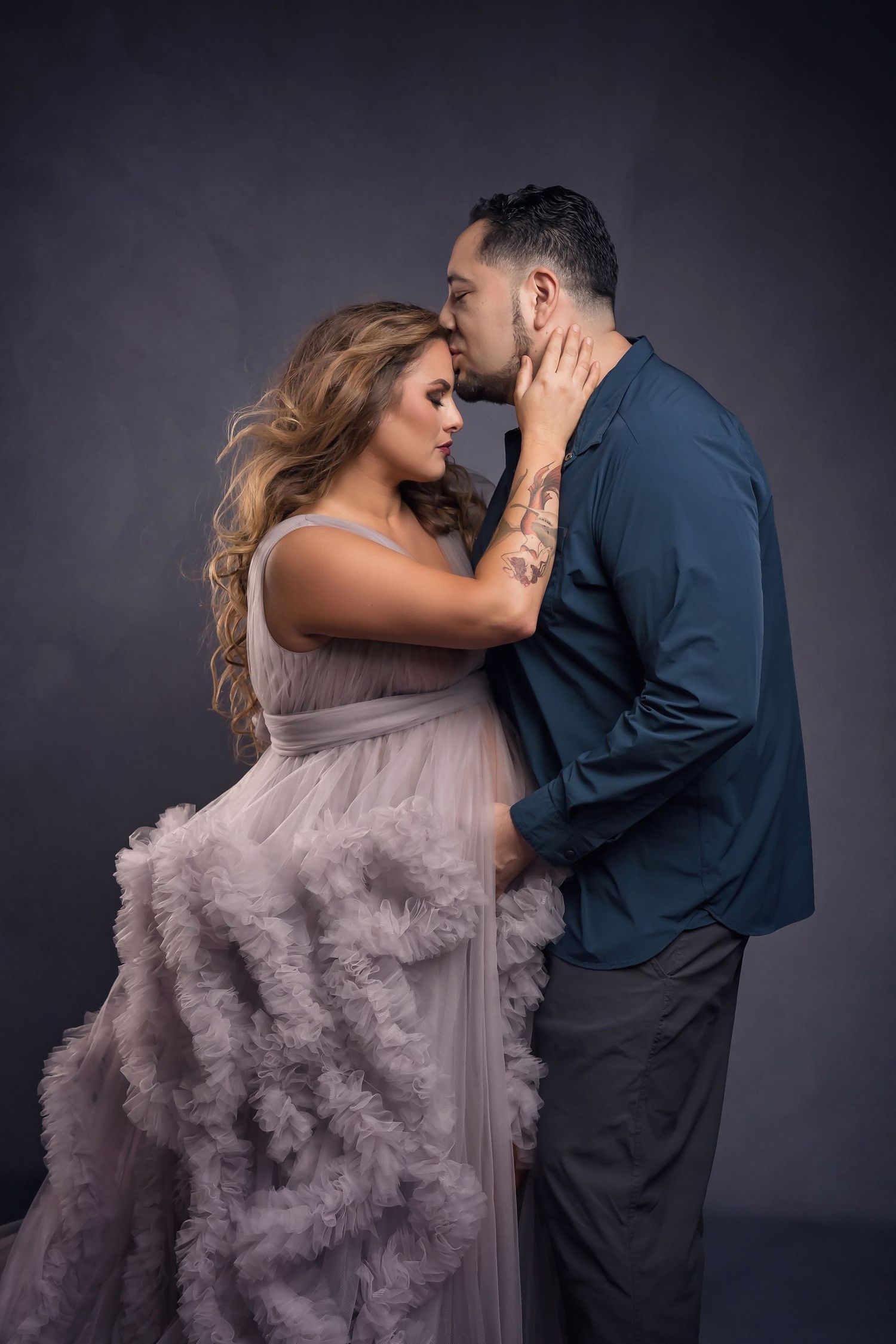 Romantic maternity couple portrait in formal attire against dark studio background