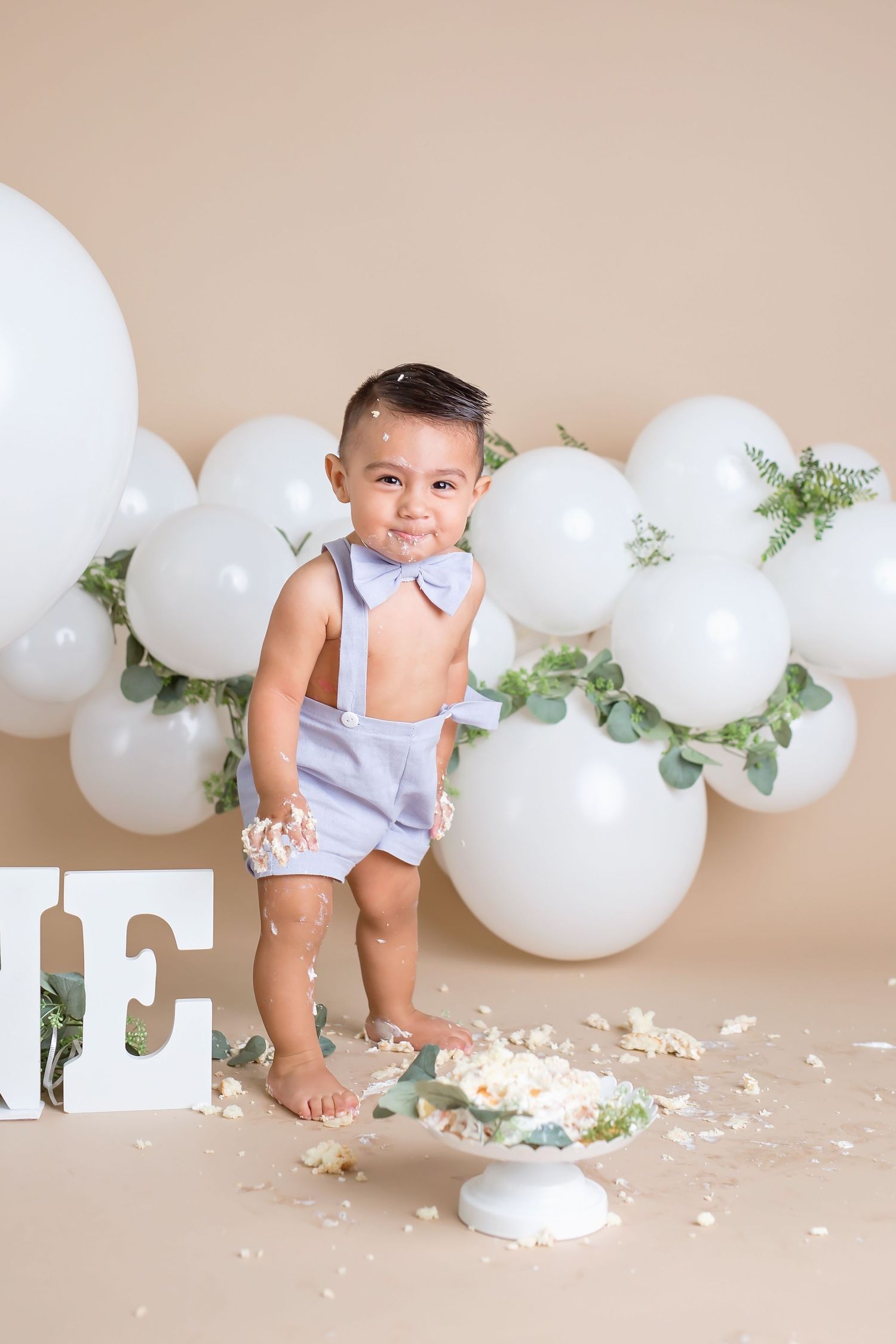 Festive white balloon garland with greenery decorates a neutral backdrop for a photo session. San Diego cake smash photographer