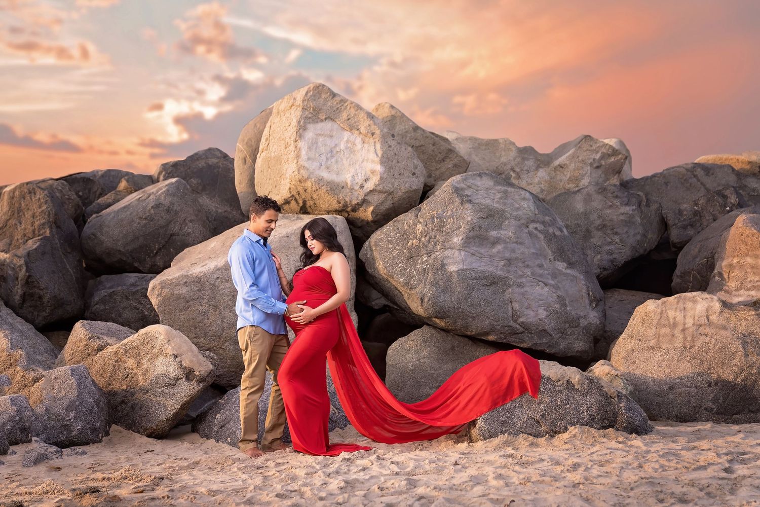 A flowing red dress creates dramatic contrast against rocky desert terrain at sunset. San Diego Maternity Photographer
