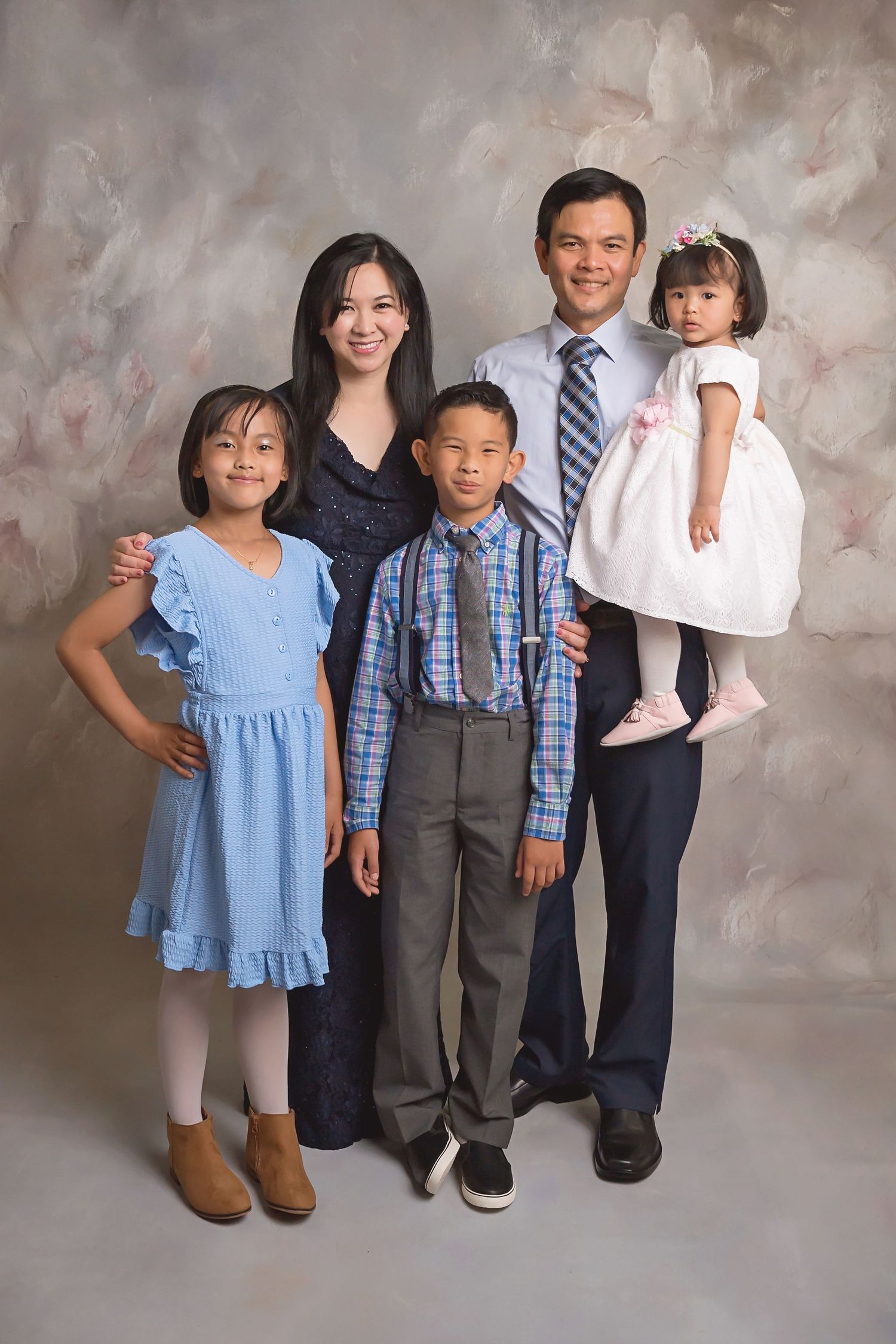 Family portrait with blue and neutral outfits posed against a textured gray studio backdrop