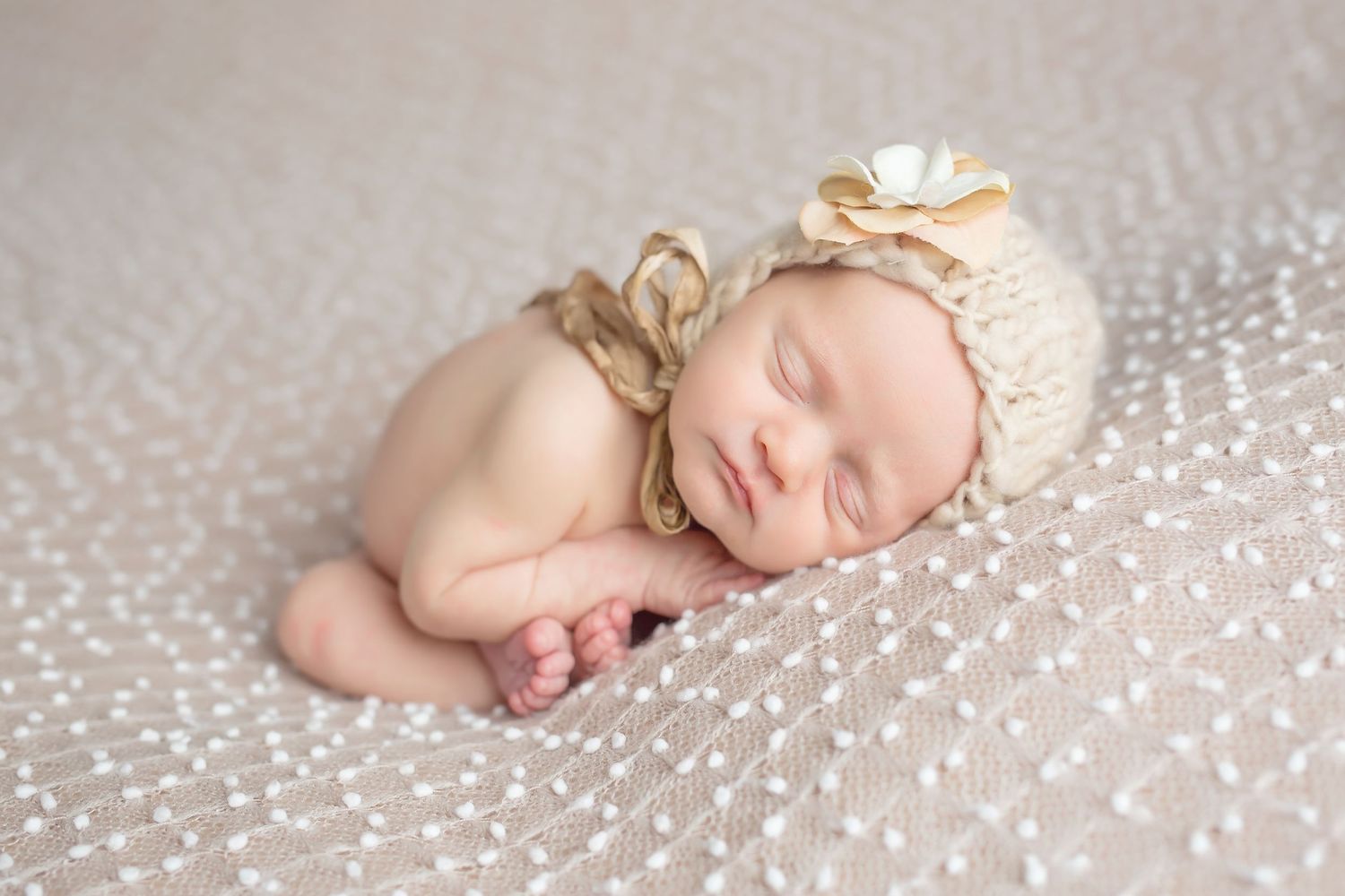 Sleeping newborn on sparkly white backdrop wearing delicate flower headpiece. San Diego Newborn Photographer