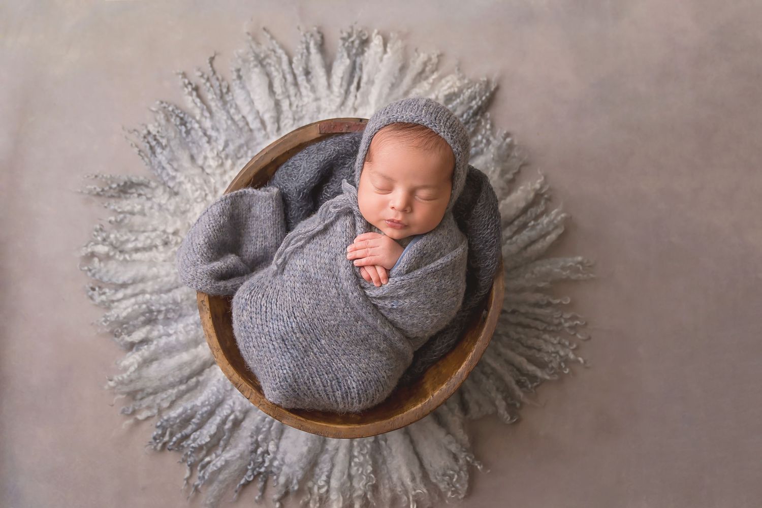 Newborn photography series showing sleeping baby in grey wrap on wooden bowl against neutral backdrop. San Diego Newborn Photographer