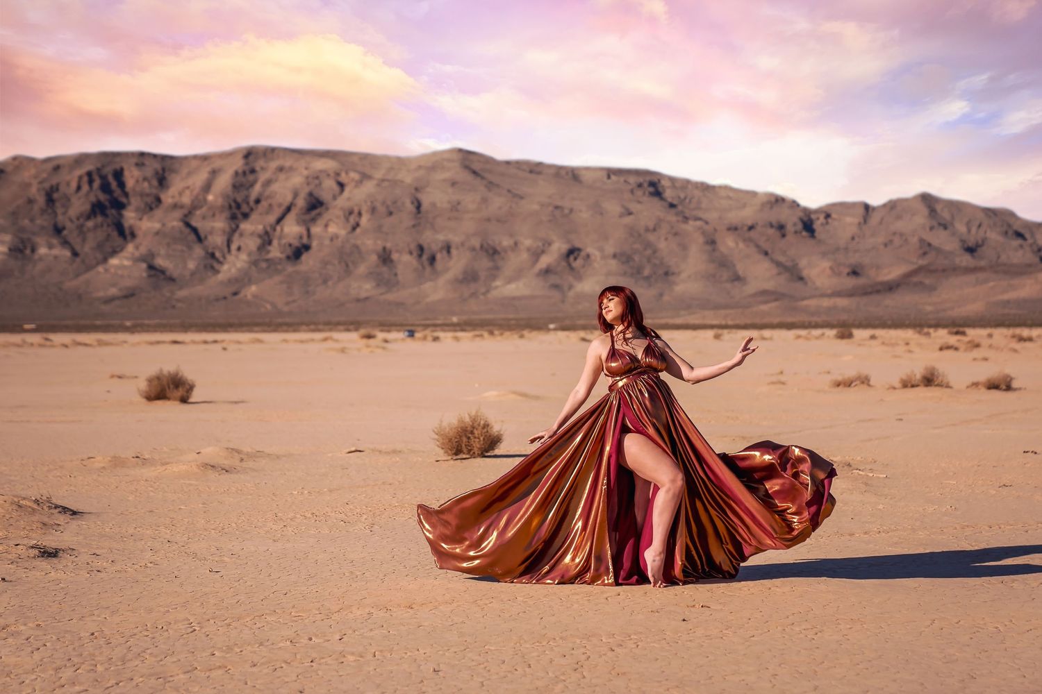 A flowing red gown creates an artistic silhouette against the desert mountains at dusk. San Diego Maternity Photographer